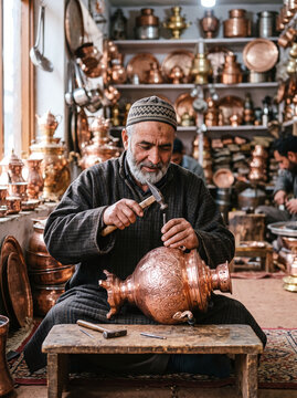 Kashmiri craftsman engraving intricate patterns on a traditional copper samovar