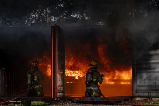 Team of firefighter in fireproof clothe with oxygen tank using twirl fog watering hose to put out the burning building with high flame for fire extinguish risk rescue mission and accident management