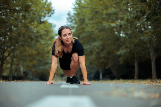  Woman Athlete In Starting Position Ready To Run On Track. Athletic female runner wearing black sportswear concentrates on starting her outdoor race