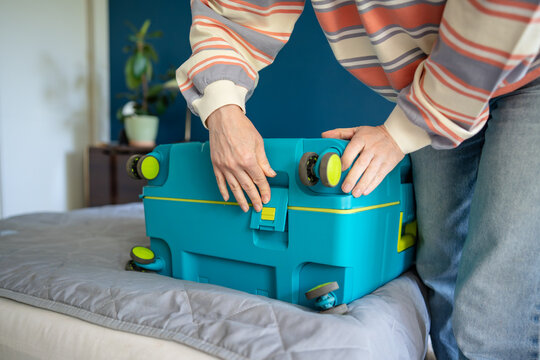 Woman closing side safety latch clip on personal suitcase packed with necessary clothing and items, female hand pressing on plastic snap lock on luggage for security traveling during long-term trip.