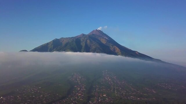Aerial drone Sunset footage of Mount Merapi active volcano towering over Selo village and clouds in Central Java, Indonesia.