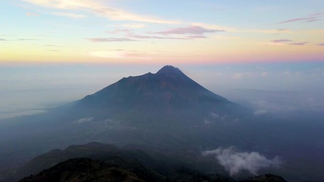Aerial drone Sunset footage of Mount Merapi active volcano towering over Selo village and clouds in Central Java, Indonesia.