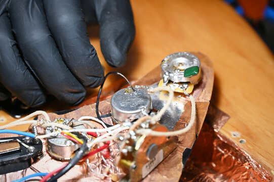 macro photograph of a guitar technician installing or soldering a potentiometer inside a copper-shielded cavity of an electric guitar