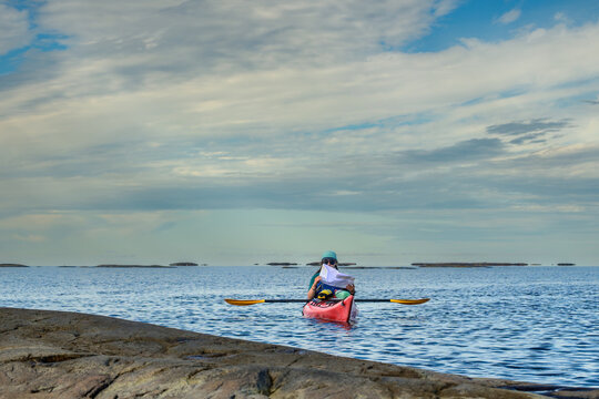 Solo sea kayaker reading a nautical chart while afloat near a granite shoreline with distant islands, blue sky copy space, Georgian Bay, Ontario