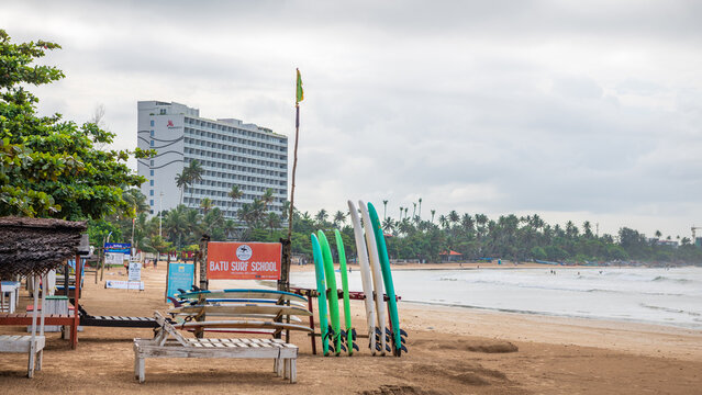 Scenic view of Weligama Beach in southern Sri Lanka, featuring colorful surfboards arranged on the sandy shore, traditional beach shelters, and a surf school