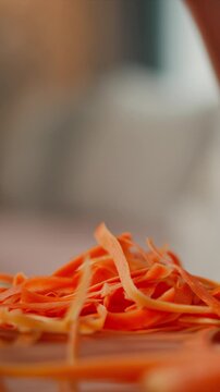 Hand with neatly manicured nails repeatedly picks up and lets go of thin carrot peels creating dynamic close up scene. bright orange color dominates frame as fresh vegetable strips