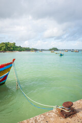Fototapeta premium traditional fishing boat is moored beside a harbor pier in Weligama, Sri Lanka, with ropes secured to a weathered metal bollard in the foreground