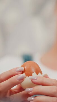 Woman hands carefully peel brown egg revealing white interior. focus remains on her fingers and cracked shell throughout sequence. Soft lighting highlights details of skin texture and nail