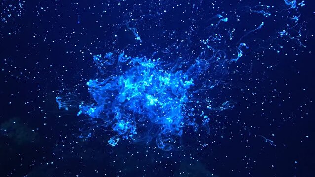 Abstract blue ink cloud exploding in dark water with tiny glowing particles