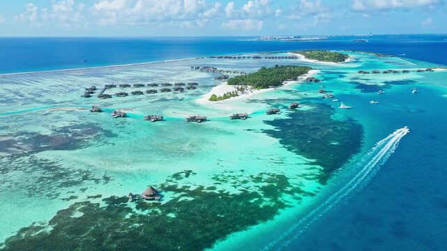 Drone shot of speedboat leaving white water wake in deep sea near paradise resort island. Dynamic visual asset for summer holiday, marine travel, and water sports promo.Maldives