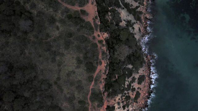 4K top-down drone view of Cap Blanc in Ibiza, Spain. Rocky formations, crystal-clear Mediterranean waters and rugged coastline create striking patterns along the coast near Es Vedr&agrave;.