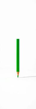 Green pencil lies flat on clean white surface, its vibrant color standing out against pure backdrop, writing, minimalistic