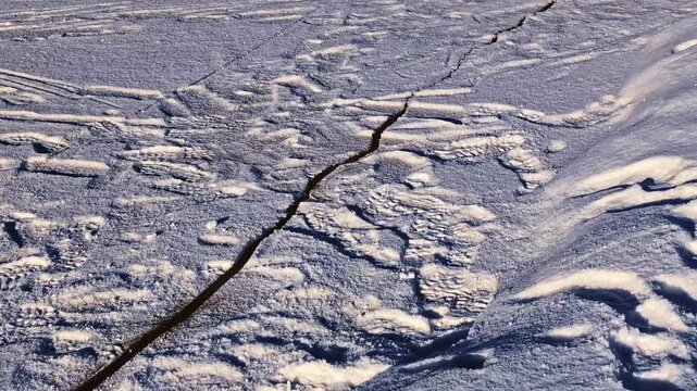 Cracked ice sheet on a frozen riverbank melting and breaking away during the spring thaw