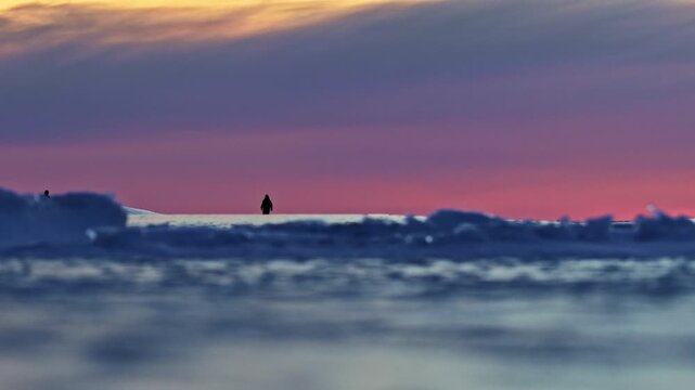 Distant people walking on an iceberg against a colorful sunset sky in a cold arctic location