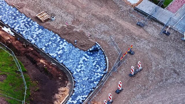 Unfinished cobblestone sidewalk and road construction site from a top-down aerial perspective