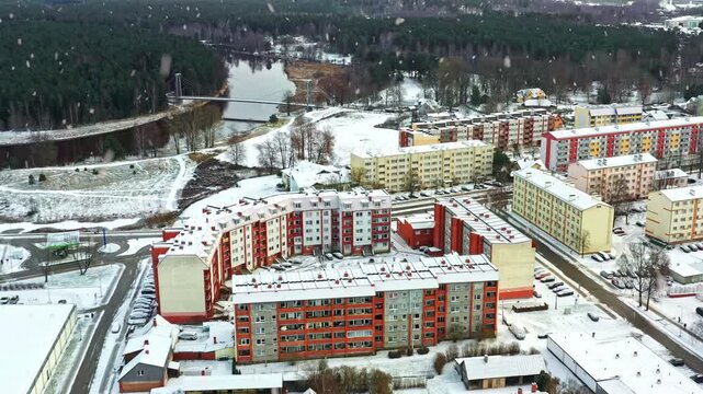 Heavy snow falling over a town with Soviet-era apartment blocks, a forest, and a river