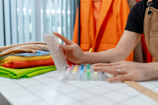 Professional fashion designer using a smartphone while managing a sewing studio and organizing tailoring supplies. Creative apparel production, small business and handmade craftsmanship.
