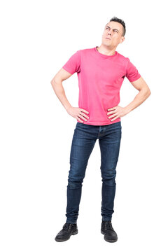 Full body of attentive young male model with dark hair in casual clothes with hands on waist and looking away with hesitation