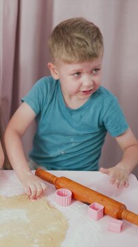 Children engage in hands on baking activity rolling and cutting dough with silicone molds. boy uses pink cupcake mold to cut shapes from rolled out pastry while another child assists nearby