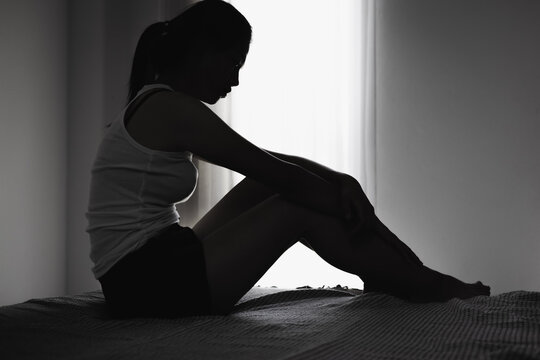 Woman sitting on bed in silhouette by window