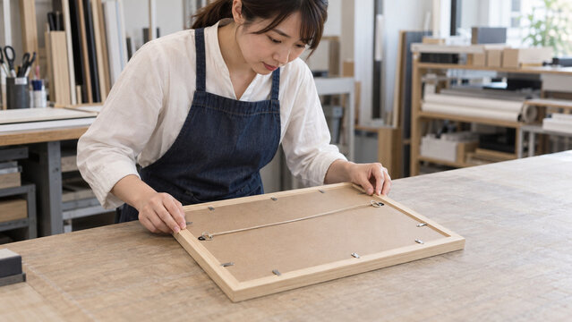 額装店で木製フレームの裏面を確認するスタッフ