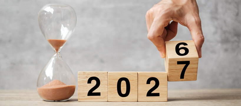 hand flipping block 2026 to 2027 text with hourglass on table. Resolution, time, plan, goal, motivation, reboot, countdown  and New Year holiday concepts