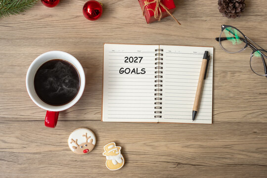 2027 GOAL with notebook, black coffee cup, Christmas cookies and pen on wood table. Xmas, Happy New Year, Resolution, To do list, Strategy and Plan concept