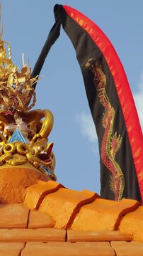 Traditional Balinese temple roof ornament with dragon flag and golden sculpture against blue sky