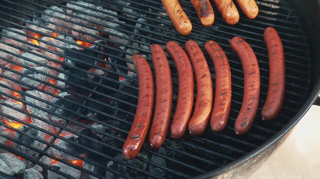 Grilled hot dogs sizzle on a kettle grill filled with coals