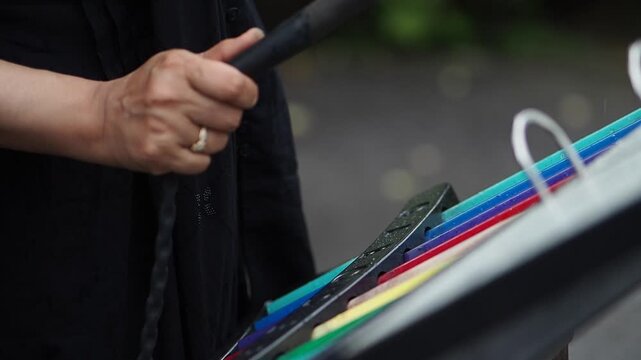 A woman uses a mallet to play a colorful musical instrument in an outdoor setting
