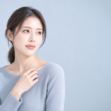 淡いブルー背景で鎖骨に手を添え透明感のある素肌を見せる日本人女性の美容ポートレート