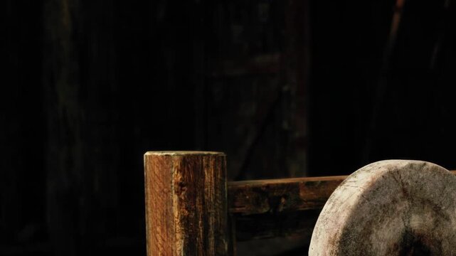 An old, weathered wooden wheel leans against a sturdy post in a dim barn. The low light highlights the textures of the wood, creating a nostalgic atmosphere.