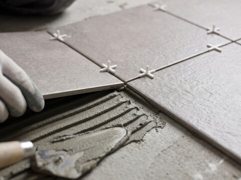 Close up of a tiler installing ceramic floor tile on fresh adhesive mortar using spacers during home renovation