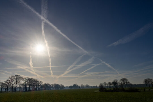 Multiple Aircraft Contrails Crossing Blue Sky Over Rural Countryside Landscape at Sunrise