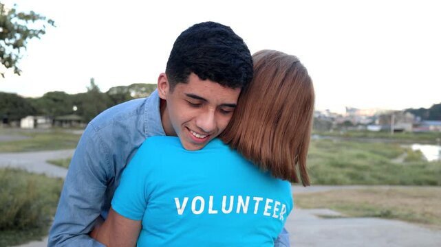 Happy hispanic teenage boy hugging volunteer at city park - Friendship, charity and community support concept