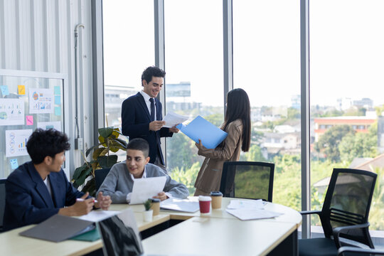 Business professional meeting in modern office showing happy teamwork and communication by window discussing corporate document together