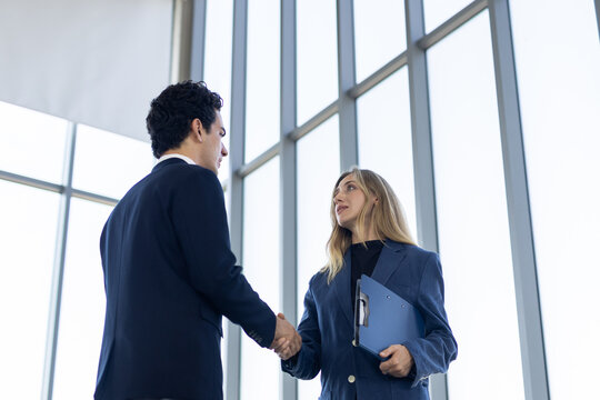 Confident business partner gives positive handshake during corporate meeting near bright window inside modern office for future success