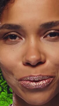 Young African American woman showcases lips covered in shimmering glitter, making kissy faces and smiling directly into the camera. Glossy textures and expressive movements highlight a vibrant look.