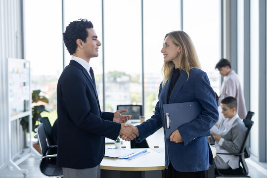 Cheerful businessman and businesswoman shaking hand in modern office with confident smile during successful corporate meeting
