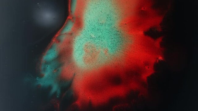 Red and teal inks collide and spread over a black surface in a pulsing organic abstract pattern for bold motion backgrounds.