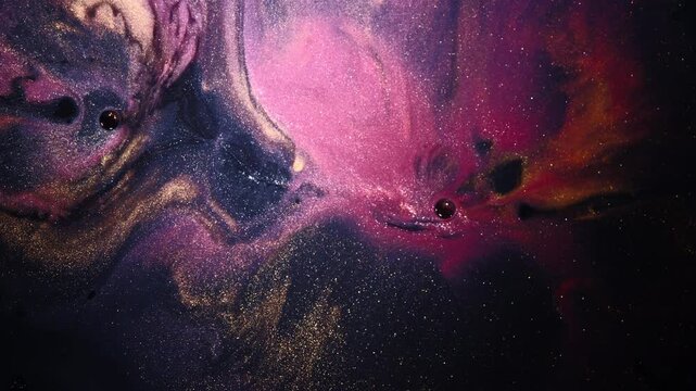 Pink, gold and purple pigments swirl through black liquid, forming a drifting galaxy-like ink cloud with glittering particles.