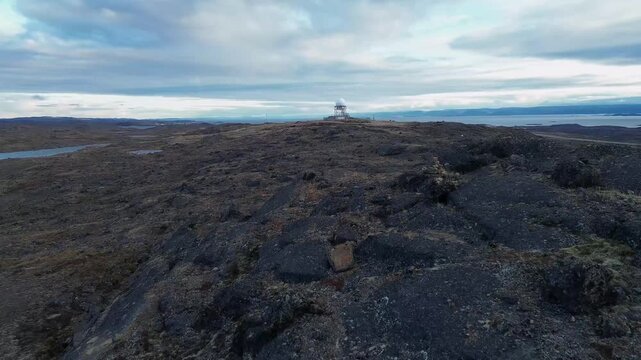 Low altitude aerial drone shot flying over dark granite tundra bedrock tracking toward hilltop radar station near Iqaluit