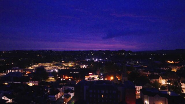 Aerial view across Salisbury at blue hour showing illuminated streets buildings and rooftops beneath a deep blue and purple evening sky