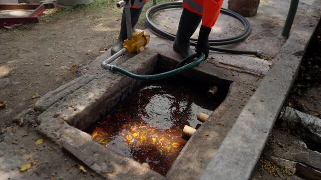 An unrecognizable worker in overalls connects a hose to a hydropump, extracting water mixed with organic residues from a pit, part of a circular agribusiness initiative.