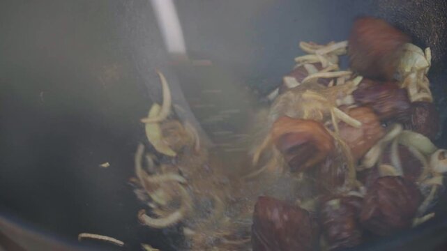 Close-up of female chef in khan atlas dress stirring meat and onions in cauldron for pilaf