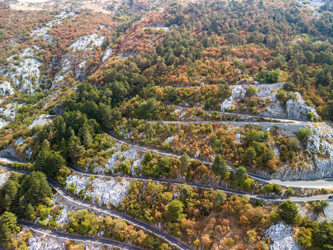 Lovcen Serpentine Montenegro winds across rocky slopes, with switchback road threading through autumn forest. Serene mountain landscape reveals rugged limestone and dense pines in vivid seasonal