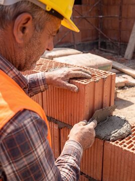 Close up of bricklayer building exterior wall with ceramic masonry blocks, construction worker applying mortar with trowel on residential construction site
