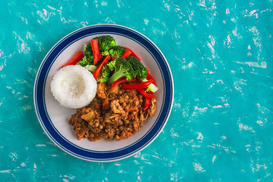 Blue-rimmed plate holds steaming rice and stir-fried veggies. Chunks of brown meat mix with broccoli and bell peppers. Bright turquoise surface adds vivid contrast to meal