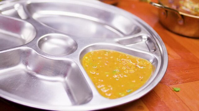 Serving Yellow Dal Curry into Stainless Steel Thali Platter