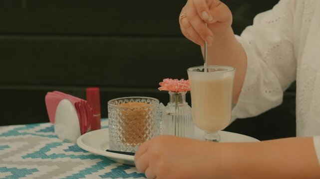 A dessert spoon is used to add sugar to a mug of drink in an outdoor caf&eacute; with a beautiful table.